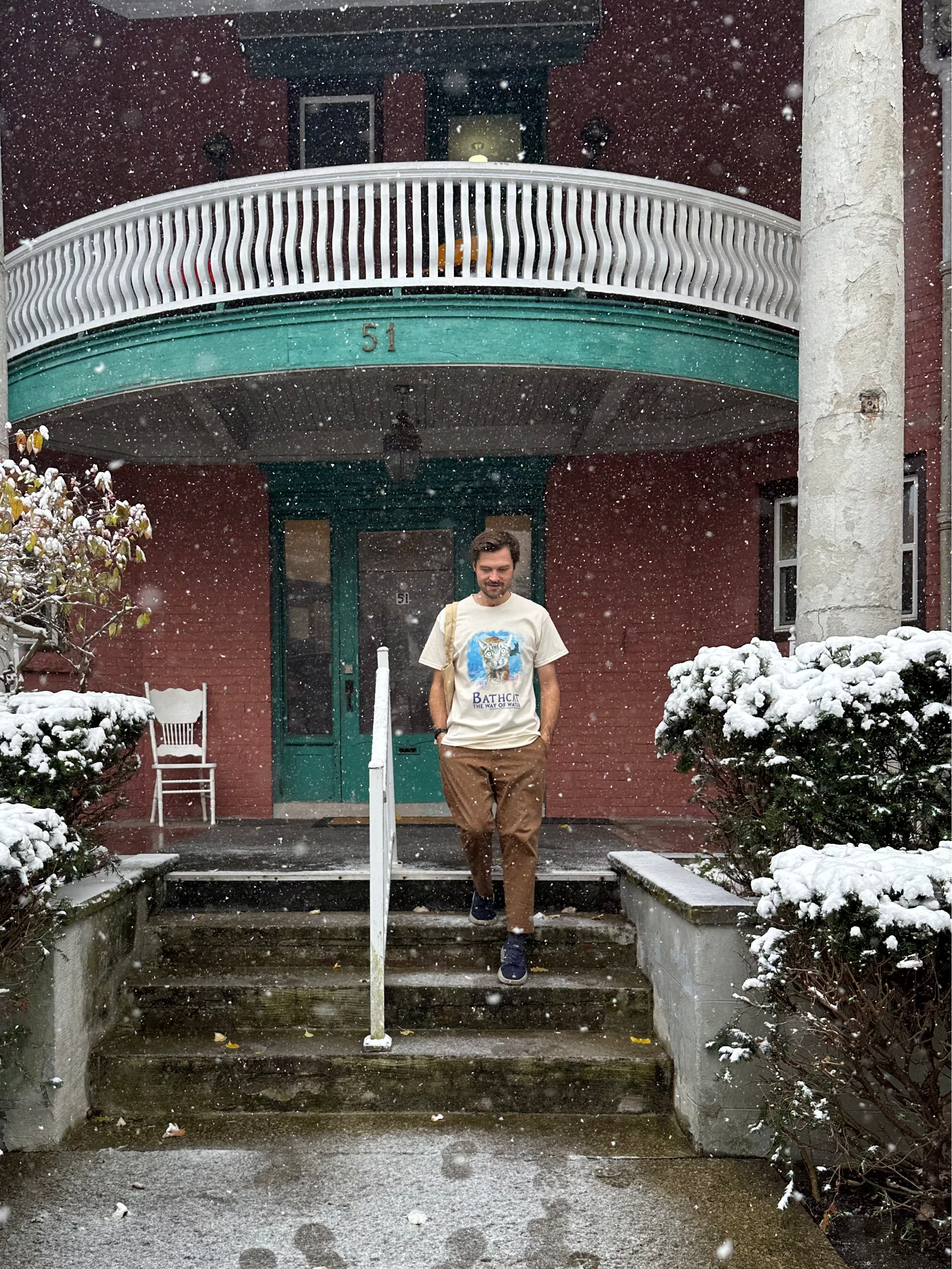 Person standing on steps in front of a house with snow falling